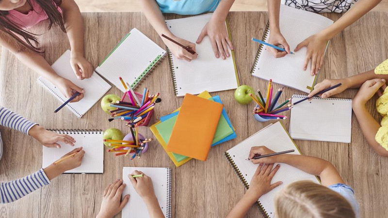 Die Kinder sitzen am Tisch und schrieben die Aufgabe.