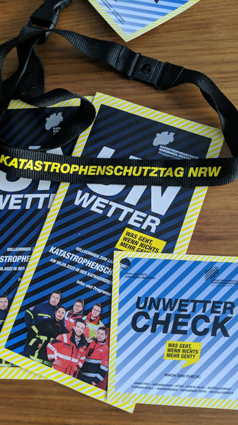 Materialien vom Katastrophenschutztag NRW. Zwei Broschüren "Unwetter" und "Unwetter-Check" und ein Schlüsselband mit dem Schrifttzug "Katastrophenschutztag"