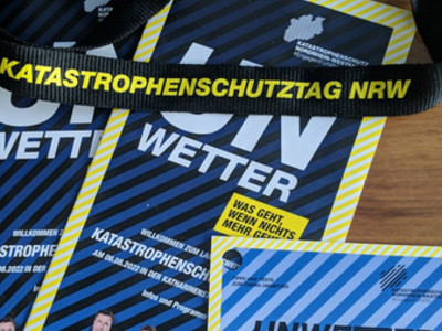 Materialien vom Katastrophenschutztag NRW. Zwei Broschüren "Unwetter" und "Unwetter-Check" und ein Schlüsselband mit dem Schrifttzug "Katastrophenschutztag"