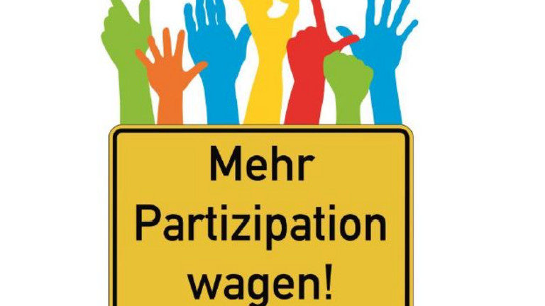 Im Bild ist ein Ortsschild mit Aufschrift "Mehr Partizipation wagen"! und über dem Schild sind Hände zu sehen. 