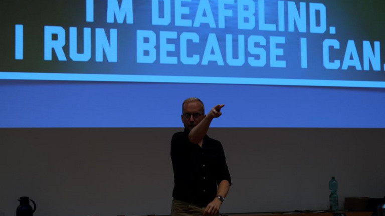 James Clarke mit Präsentationshintergrund "I´m deafblind. I run because I can."
