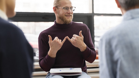 Ein Mann eklärt taube Eltern das Thema Elternassistenz in DGS