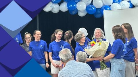 Frau Bagus bekommt die Blummen für Ihre Arbeit. Mitarbeiter*innen vom Team stehen und gratulieren Ihr erfolgreiche Zusammenarbeit.