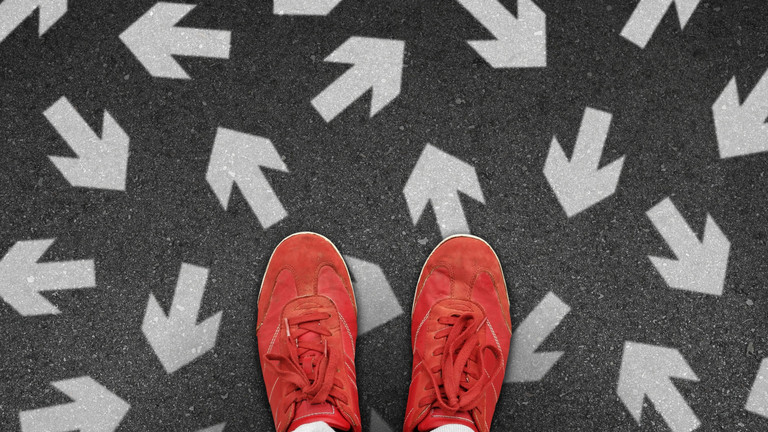 Zwei Füße stehen nebeneinander auf dem Boden. Auf dem Boden sind Pfeile  gezeichnet. Diese zeigen in verschiedene Richtungen