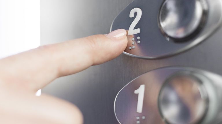 Zeigefinger drückt auf Fahrstuhlknopf mit Brailleschrift.