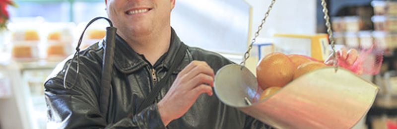 Blinder Mann beim Einkauf legt Obst auf Waagschale